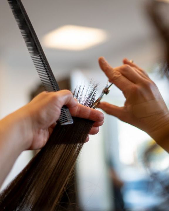 Mani di parrucchiera che tagliano una ciocca di capelli con pettine e forbici